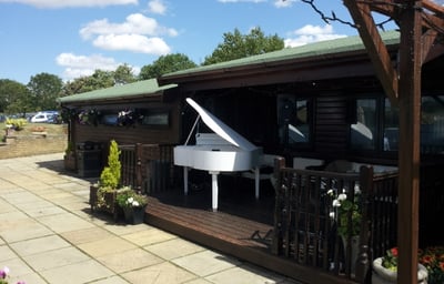 A wedding ceremony outside with the grand piano at Flaxbourne Gardens