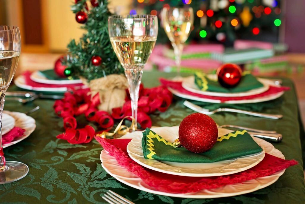 A table set for a Christmas dinner with glasses of fizz, red baubles and a lit tree behind